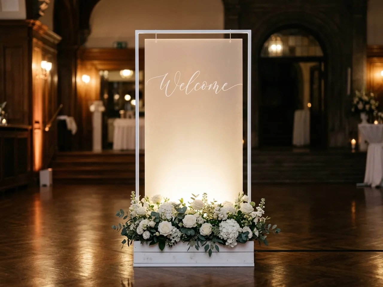 Beleuchtetes weißes Empfangsschild mit Blumenkasten am Eingang einer Abendveranstaltung